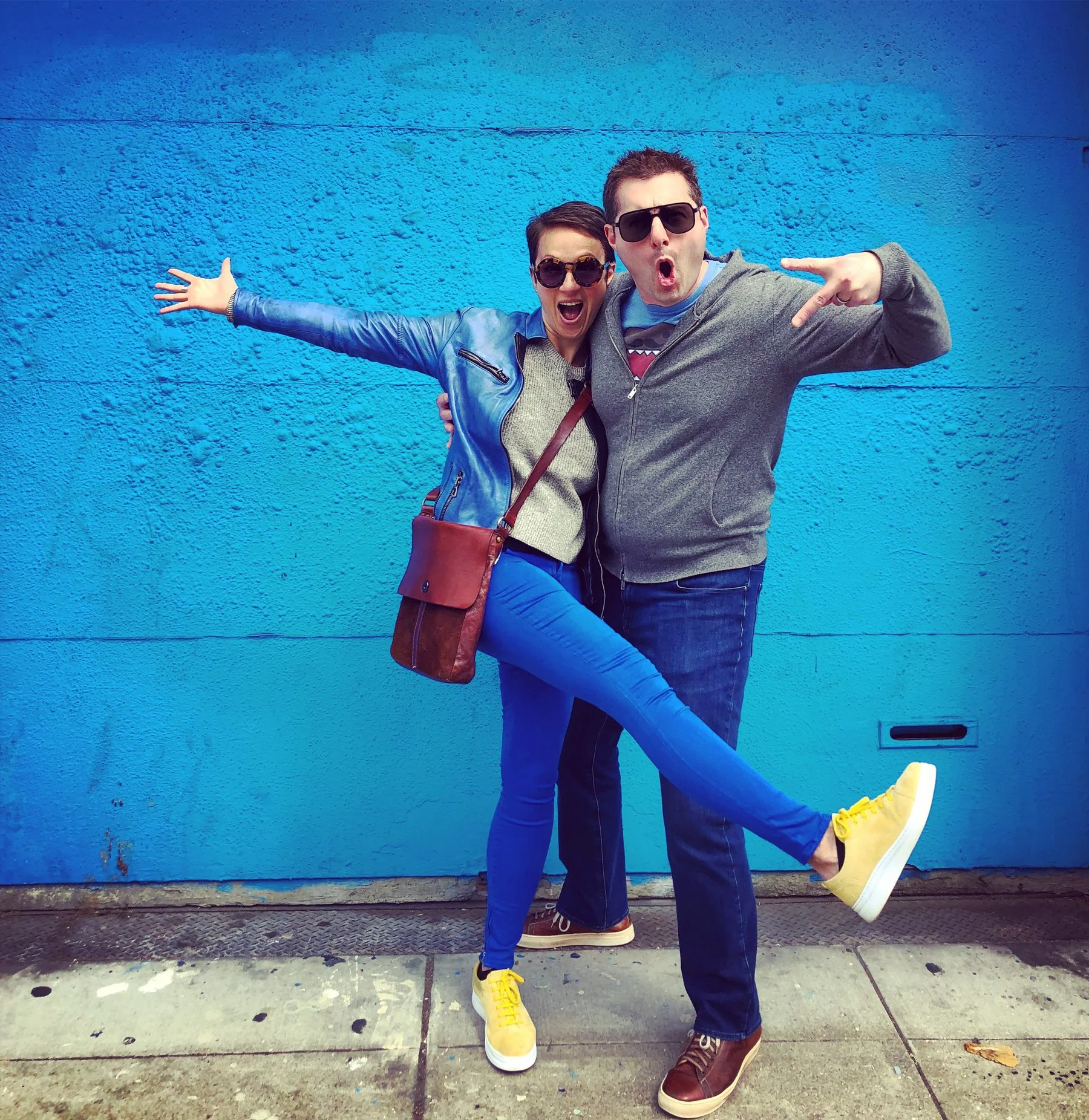Nataly Kogan and Avi Spivack striking playful poses in front of a bright blue wall