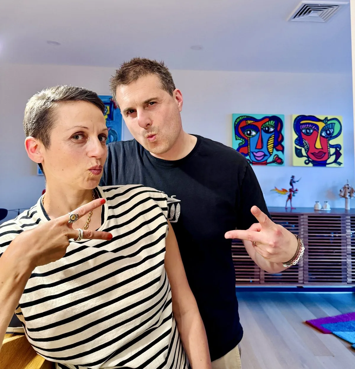 Nataly and Avi at home, striking playful poses in front of Nataly's paintings